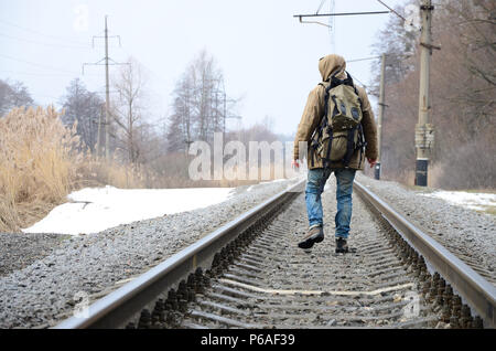 Ein Mann mit einem großen Rucksack geht weiter auf der Bahntrasse in der Wintersaison. Stockfoto