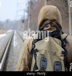 Ein Mann mit einem großen Rucksack geht weiter auf der Bahntrasse in der Wintersaison. Stockfoto