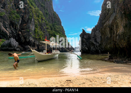 Ein Mann zieht ein Boot am Strand gegen das Meer und die Klippen in der wunderschönen Lagune auf der Insel Palawan auf den Philippinen Stockfoto