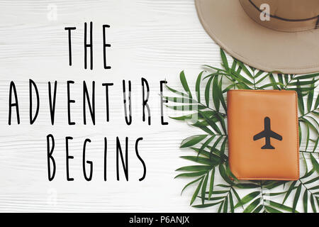 Das Abenteuer beginnt, Text auf Passport mit Flugzeug und Hut mit grünen Palmen Blätter auf weißem Hintergrund Holz. Moderne Sommerferien Bild, stilvollen Flachbild Stockfoto