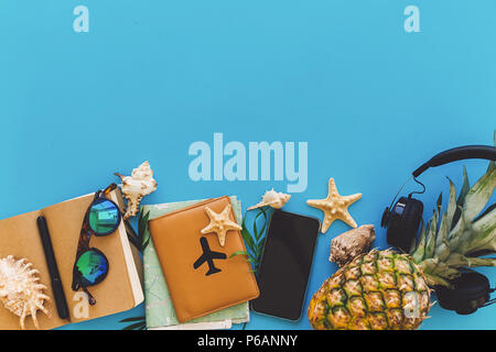 Sommer Urlaub und Reisen flach. Elegante schwarze Telefon, Reisepass, Sonnenbrille, Karte, Ananas mit Kopfhörer, Muscheln, Notebook am trendigen blau Papier. Stockfoto