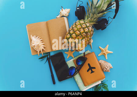 Planung Sommer Urlaub flach. Elegante schwarze Telefon, Reisepass, Sonnenbrille, Karte, Ananas mit Kopfhörer, Muscheln, Notebook am trendigen blau Papier. sp Stockfoto