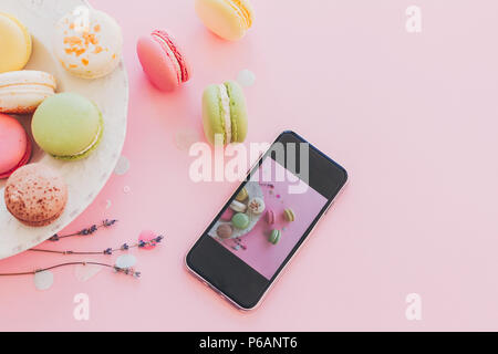 Moderne Nahrungsmittel fotografie Konzept. Telefon mit Foto von stilvollen bunte Makronen in vintage Platte am trendigen rosa Papier mit Lavendel. Platz für Text. Stockfoto
