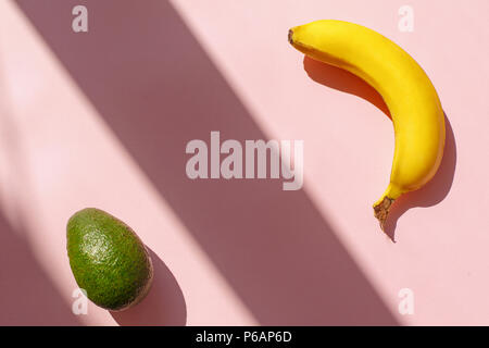 Saftige avocado und Banane auf trendigen rosa Papier Hintergrund in der Sonne Licht. Flach. Kreative kontrast Sommer Bild. Ferienhäuser und Diät Konzept. Platz für Stockfoto