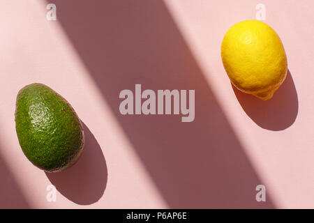 Saftige avocado und Zitrone auf trendigen rosa Papier Hintergrund in der Sonne Licht. Flach. Kreative kontrast Sommer Bild. Ferienhäuser und Diät Konzept. Platz für t Stockfoto