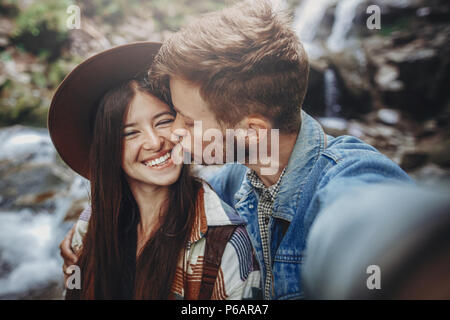 Happy hipster Paar unter selfie am Wasserfall im Wald. stilvolle Familie reisen, umarmen und küssen. glückliche Momente. Platz für Text. Reisen und Stockfoto