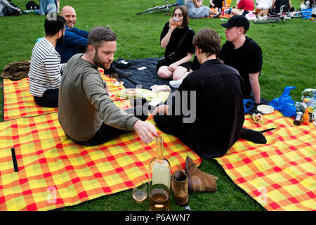 London. Hackney. London Felder. Grillfeste und Picknicks. Eine Gruppe junger Leute, sitzen auf bunten Decken; trinken Wein aus einer übergroßen Flasche Stockfoto