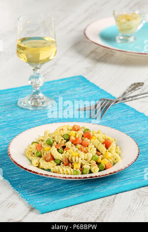 Leckere hausgemachte Fusilli mit Basilikum Pesto, Karotten, mais und Erbsen in einer Platte auf einem türkis blau serviette gekocht, serviert mit einem Glas weiß Win Stockfoto