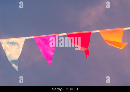 Dreieckige Flaggen verschiedener Farben werden in einem Seil genäht und im Wind wiegen gegen den Himmel. Verschwommen Stockfoto