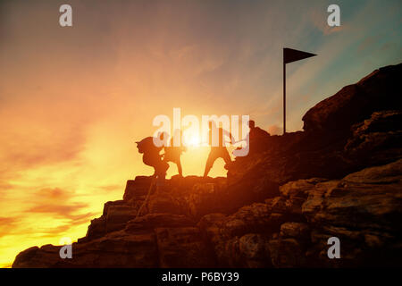 Silhouette männlichen und weiblichen Wanderer klettern Klippe, hilft und Arbeiten im Team. Stockfoto