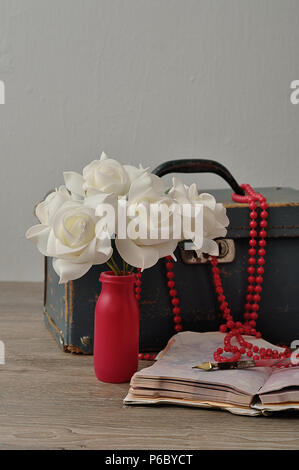 Eine alte abgenutzte blaue Koffer mit einer Reihe von künstlichen weissen Rosen, ein String rosa Perlen, ein Notizbuch und Stift Stockfoto