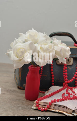 Eine alte abgenutzte blaue Koffer mit einer Reihe von künstlichen weissen Rosen, ein String rosa Perlen und eine Notiz Buch Stockfoto