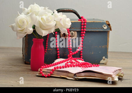 Eine alte abgenutzte blaue Koffer mit einer Reihe von künstlichen weissen Rosen, ein String rosa Perlen und eine Notiz Buch Stockfoto