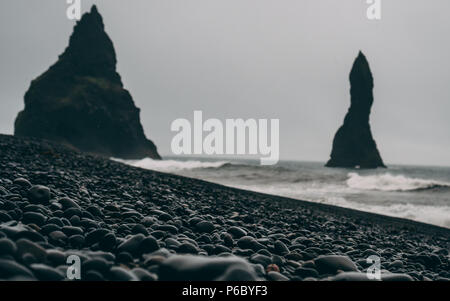 Schwarze Steine mit Küste und großen schwarzen Felsen in Island Stockfoto