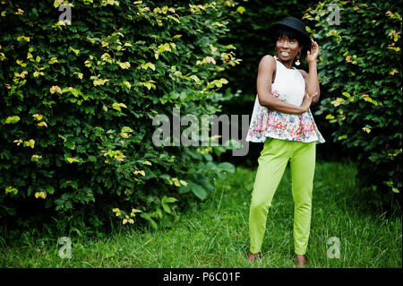 Erstaunlich afrikanische amerikanische Modell Frau in grüne Hosen und schwarzen Hut Stellen im Park. Stockfoto