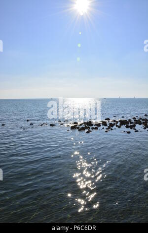 Sonne im Meer widerspiegelt, wie mit schwarzen Steinen in der Mitte Funken Stockfoto