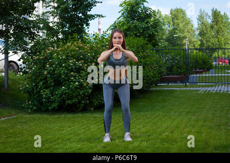 Eine dunkelhaarige Frau Trainer in einem sportlichen kurzen Top und Fitnessraum leggings zeigt die richtige Besetzung Technik, in der Ausgangsposition, Hände vor der Hi Stockfoto