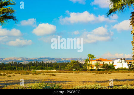 Landschaft der Stadt Paphos mit Häuser, Bäume und Berge im Hintergrund gegen den blauen Himmel, Zypern. Fotos warmen Farben der untergehenden Sonne Stockfoto