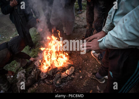 Flüchtling versuchen sich zu warm und trocken Sie feuchte Tücher vom Lagerfeuer nach einem Regen Nacht im provisorischen Flüchtlingslager der Greek-Macedonian bord Stockfoto