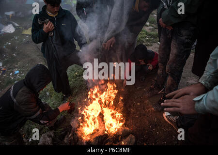 Flüchtling versuchen sich zu warm und trocken Sie feuchte Tücher vom Lagerfeuer nach einem Regen Nacht im provisorischen Flüchtlingslager der Greek-Macedonian bord Stockfoto