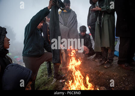 Flüchtling versuchen sich zu warm und trocken Sie feuchte Tücher vom Lagerfeuer nach einem Regen Nacht im provisorischen Flüchtlingslager der Greek-Macedonian bord Stockfoto