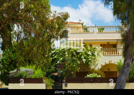 Fassade des Hauses mit Terrasse mit blühenden Busch und Garten um gegen den blauen Himmel Stockfoto