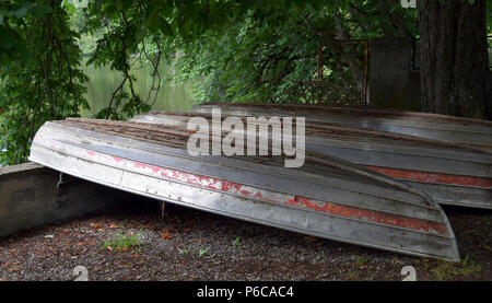 Alt und morsch Ruderboot auf den Kopf von Metall und Holz liegend vernachlässigt, drei umgedrehten Boote liegen am Ufer im Schatten eines Baumes Stockfoto