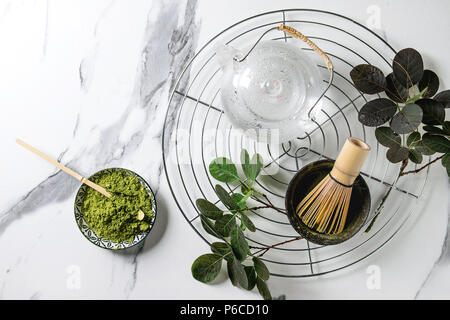 Zutaten für die Herstellung von Matcha Tee trinken. Grüner Tee matcha Pulver in Keramik Schüssel, traditionelle Bambus Löffel, Schneebesen auf Kühlung Rack, Teekanne aus Glas, grün Bh Stockfoto