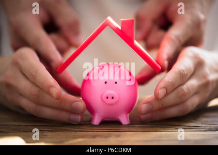 In der Nähe von zwei Menschen schützen rosa Sparschwein mit rotem Dach Stockfoto