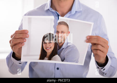 Close-up In eines Mannes Hand reißen Foto von lächelnden Paar in zwei Stücke Stockfoto