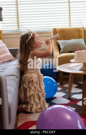 Cute girl Blasen einer Partei Horn im Wohnzimmer Stockfoto