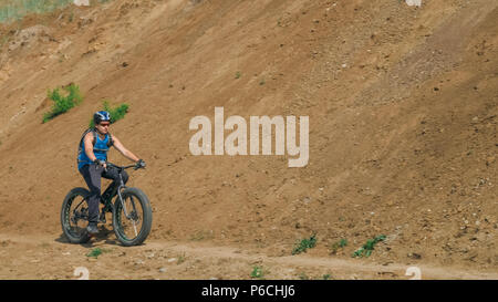 Fat bike auch fatbike oder Fat Tire Bike Im Sommer fahren auf der Straße. Der Kerl Fahrten durch die Hügel, der auf einem sand Ton weg, hinter ihm die Ufer durch. Stockfoto