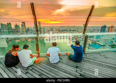 Singapur - Mai 3, 2018: die Menschen sitzen auf der Terrasse ejoying Panoramablick von der Aussichtsplattform Skypark von Marina Bay Sands Hotel und Casino. Bankenviertel Skyline im Hintergrund. Abendlicht. Stockfoto