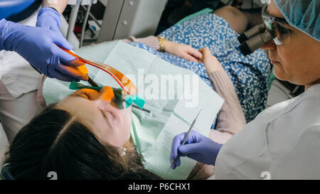 Frau beim Zahnarzt Klinik erhält der zahnmedizinischen Behandlung ein Loch in einen Zahn zu füllen. Zahnersatz und Verbundmaterial Polymerisation mit UV-Licht und Stockfoto