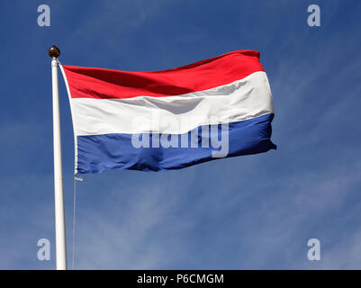 Die Flagge der Niederlanden fliegt im Wind ein blauer Himmel gegen. Stockfoto