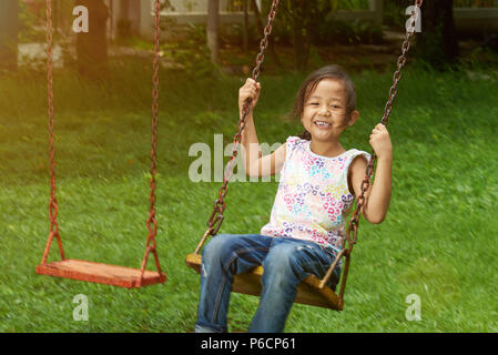 Wenig asiatisches Mädchen schwingen in Tag park Hintergrund Stockfoto