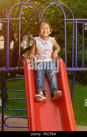 Wenig asiatisches Mädchen auf dem Spielplatz. Gerne asiatische Mädchen gleiten in Park Stockfoto