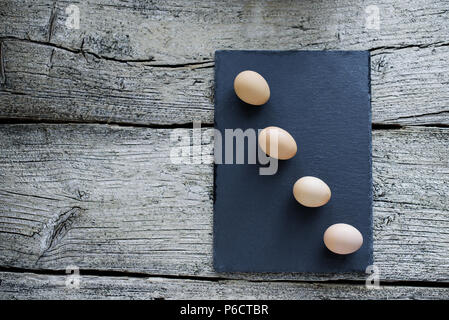 Vier rohem Huhn Eier liegen auf einem schwarzen Brett auf einem hölzernen Hintergrund. Stockfoto
