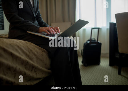 Geschäftsfrau mit Laptop am Bett im Hotelzimmer Stockfoto