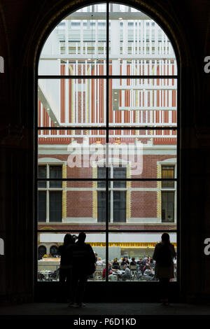 Amsterdam, Niederlande - Mai 2018: Leute, die über ein großes Fenster auf die Besucher in der modernen Halle im neuen Atrium des Rijksmuseum. Eingang zum Museum, massive Decke Dekorationen und Leute in Holland National Museum. Stockfoto