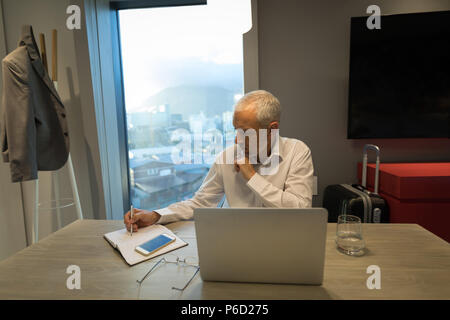 Geschäftsmann schreiben Hinweise zum Tagebuch am Schreibtisch Stockfoto