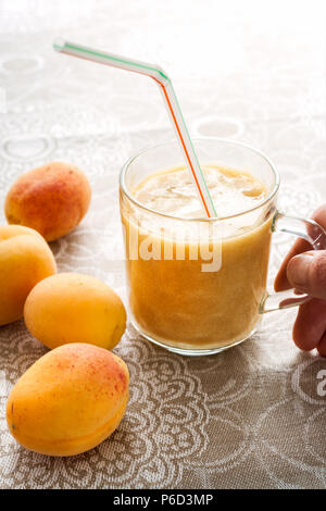 Aprikosen und Smoothie in Glas auf Leinen Tischdecke und der Frau Hand, denn ein Glas. Stockfoto