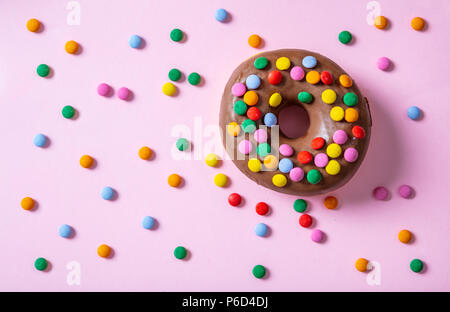 Gebäck Konzept. Donut mit Schokoladenüberzug mit Streuseln, Ansicht von oben und isoliert, auf rosa Hintergrund. Stockfoto