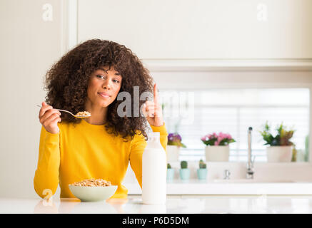 Afrikanische amerikanische Frau, Essen, Getreide und Milch zu Hause mit einer Idee oder Frage Zeigefinger mit glücklichen Gesicht überrascht, Nummer eins Stockfoto