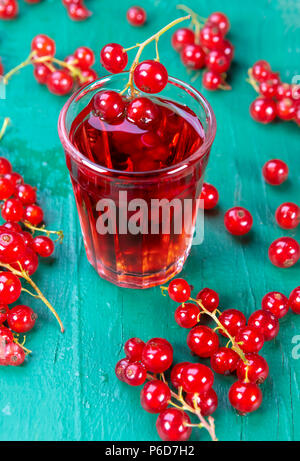 Rote Johannisbeere und Glas mit Obst und Getränk Saft auf Holz Tisch. Fokus auf rote Johannisbeere im Glas, Stockfoto