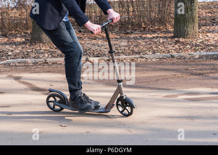 Der Junge auf dem Roller Fahrten entlang der Straße, dem Radweg Stockfoto