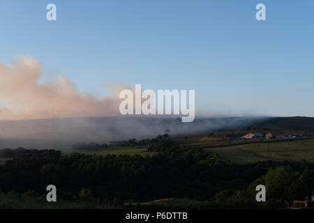 West Pennine Moors, UK, 29. Juni 2018. Gras Brände immer noch über die West Pennine Moors im Winter Hügel mit einem Bauernhof in der Nähe und vor dem Feuer. Stockfoto