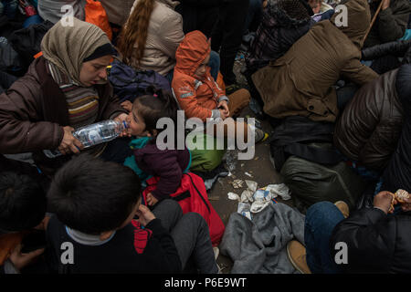 Mutter gibt ihr Kind Wasser aus einer Flasche zu trinken, in der Nähe des Gate, wie sie warten die Greece-Macedonia Grenze in den provisorischen Flüchtlingslagern zu überqueren, Ca Stockfoto