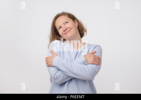 Portrait von mittleren Alters hübsche Frau im blauen Pullover vorgibt, wie sie selbst ist das Umarmen. Stockfoto