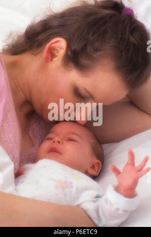 Mutter und Neugeborenes Baby im Bett mit Mama lächelnd und küssen Kind wie das Baby Fusses Stockfoto